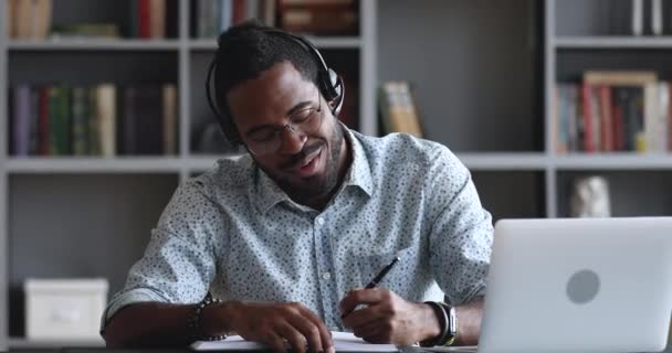 Sonriente africano masculino estudiante usar auriculares elearning haciendo notas — Vídeo de stock