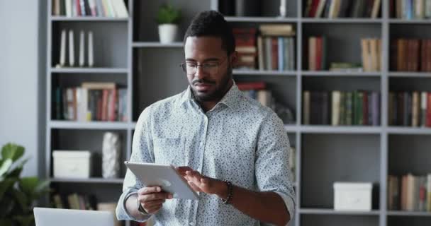 Empresário africano focado segurando usando tablet digital no escritório — Vídeo de Stock