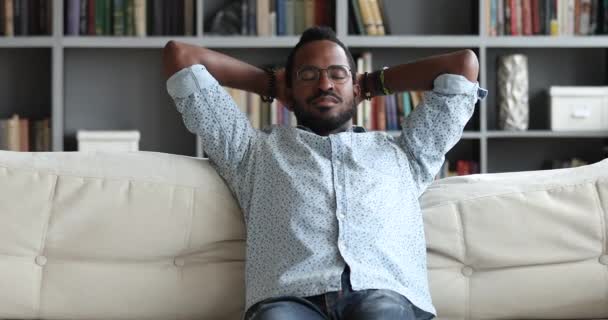 Serene young african man relax on sofa hands behind head — Stock Video