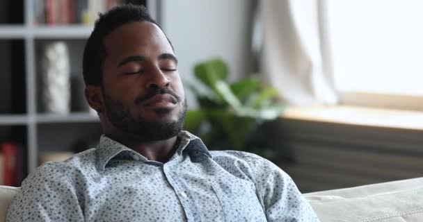 Kalme jonge Afrikaanse man mediteren op de bank met gesloten ogen — Stockvideo