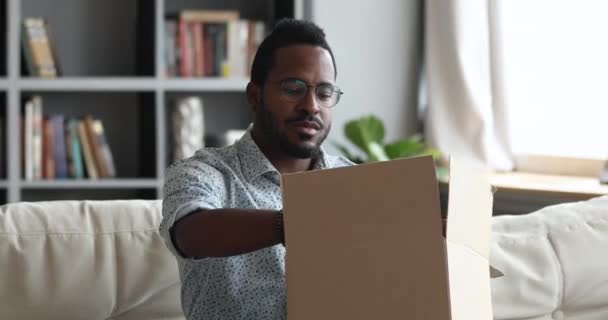 Ενθουσιασμένος αφρικανός αρσενικός πελάτης που λαμβάνει το άνοιγμα κιβωτίων δεμάτων στο σπίτι — Αρχείο Βίντεο
