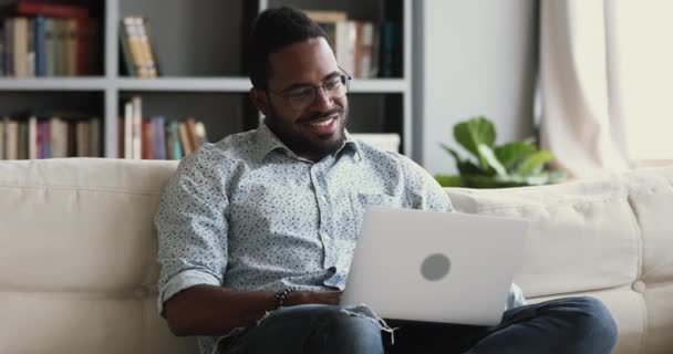 Heureux homme africain utilisant un ordinateur portable sur le canapé se détendre avec la technologie — Video