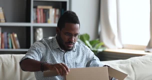 Frustrated dissatisfied african man open cardboard box receive bad parcel — Stock Video