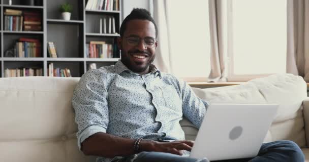 Felice uomo africano utilizzando computer portatile navigazione internet sedersi sul divano — Video Stock