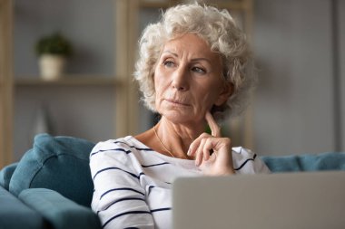 Kanepede dizüstü bilgisayarla oturan düşünceli yaşlı kadın başka yere bak.