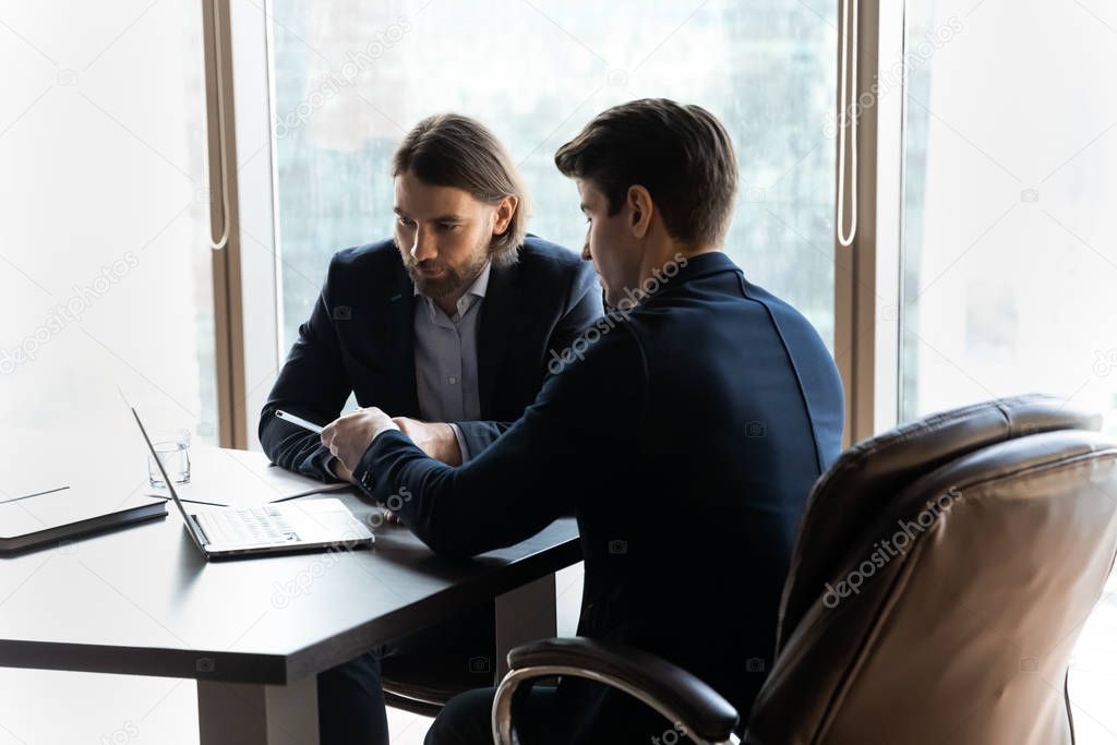 Concentrated businessmen discuss ideas cooperating at laptop