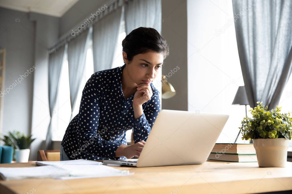 Thoughtful serious indian woman working on laptop thinking solving problem