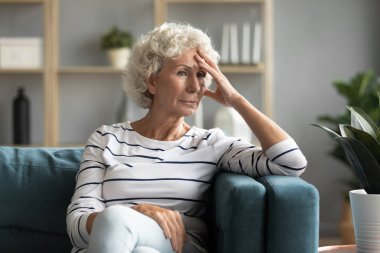 70 'lerin kadını koltukta oturmuş hayatın zorluklarını düşünüyor.