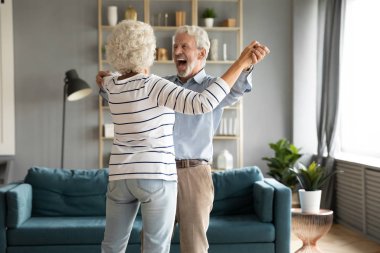 Heyecanlı yaşlı eşler sıcak oturma odasında el ele tutuşup dans ediyorlar.