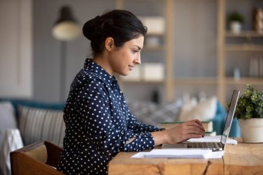 İnternette dizüstü bilgisayar kullanan Hintli bir kız masada oturuyor.