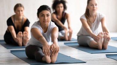 Grup dersinde yoga yapan Hintli kadın, öne eğilip eğilmiş.
