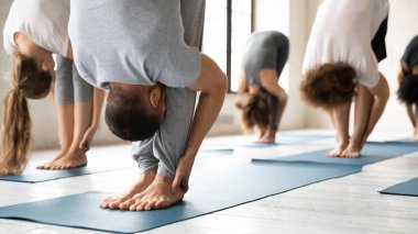 Grup dersinde yoga yapanlar, uttanasana pozu verenler.