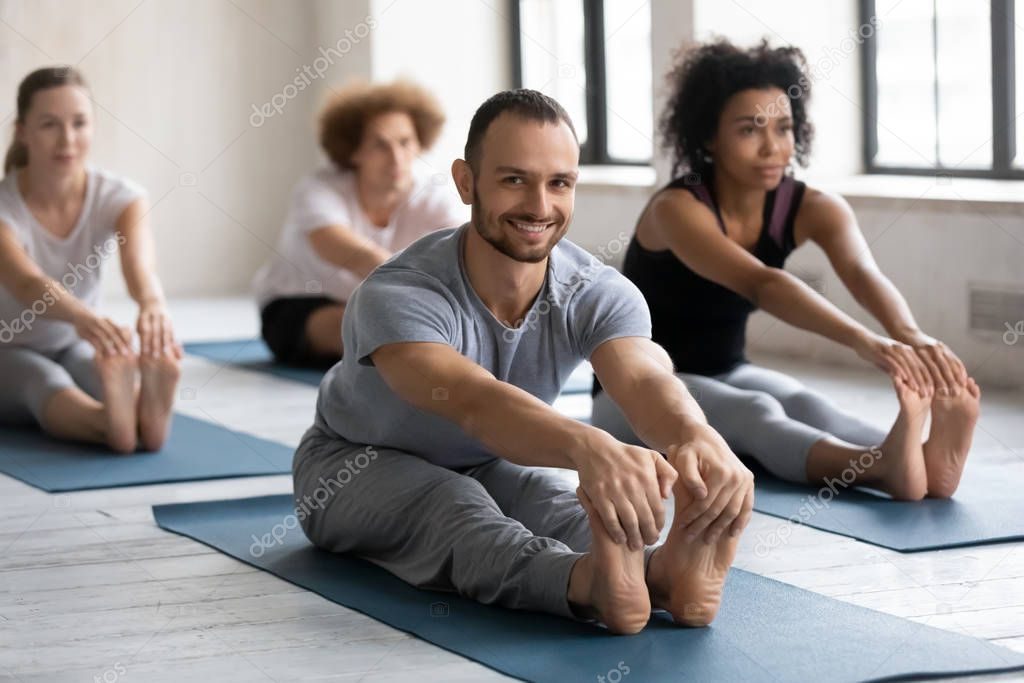 Smiling man practicing yoga at group lesson, Seated forward bend