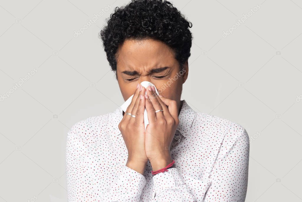 African woman holding tissue blowing running nose studio shot