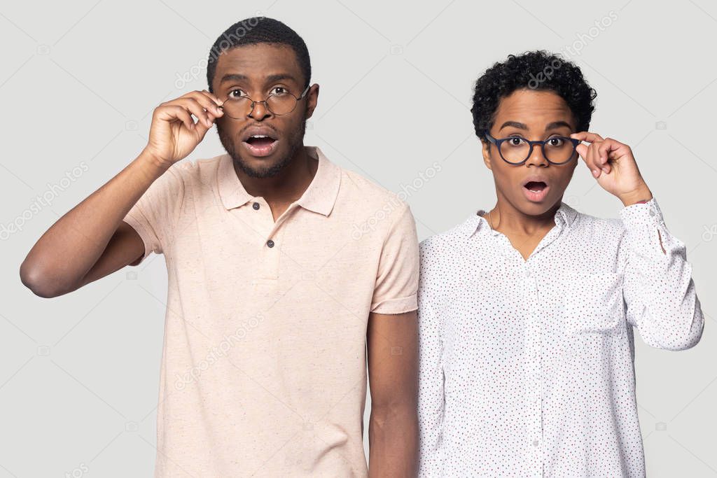 Confused african couple gawp at camera open mouth lowering glasses