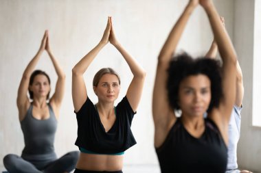 Grup dersinde yoga yapan genç bir kadın Padmasana egzersizi yapıyor.