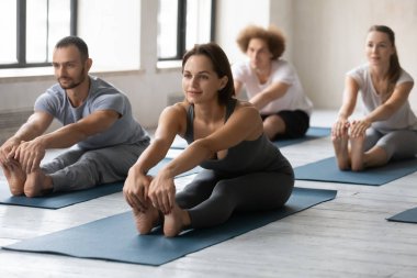 Grup dersinde yoga yapan kadın, öne eğilip eğilme egzersizi yapıyor.