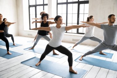 Çeşitli gençler Virabhadrasan egzersizi yapıyor, yoga yapıyorlar.