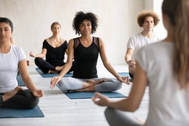 Kadın koç çeşitli insanları eğitiyor, yoga yapıyor, Padmasana egzersizi yapıyor.