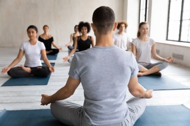 Yoga öğretmeni çeşitli insanları eğitiyor, Padmasana egzersizi yapıyor.
