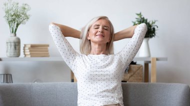 Happy elderly woman relax on sofa at home clipart