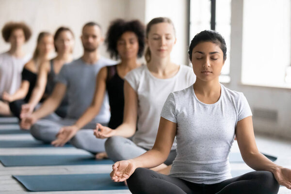 Beautiful Indian woman meditating at group lesson, practicing yoga