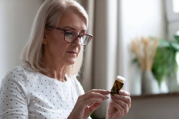 Senior woman reading medicines instruction on pills bottle — Stock Photo, Image