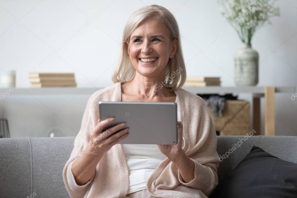 Happy senior woman smiling using tablet at home