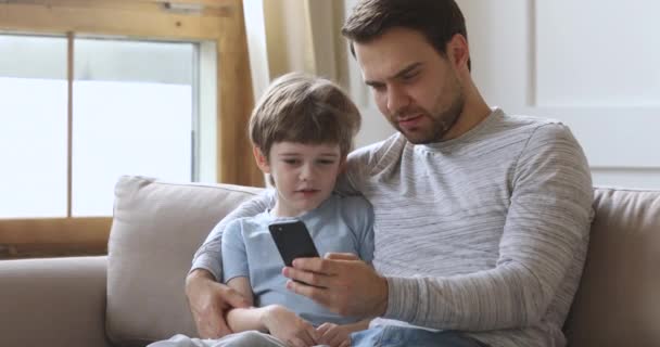 Dad teach kid son using phone having fun on sofa — Stock Video