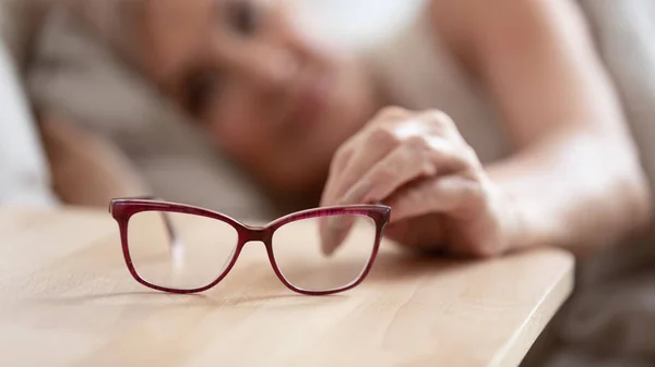 Close up of senior woman take glasses form bedside table — Stock Photo, Image