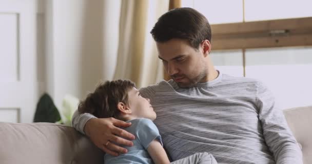 Догляд за татом, який обіймає дошкільного сина, що має довірчу розмову на дивані — стокове відео