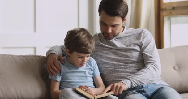 Заботливый папа учит сфокусированный дошкольный ребенок сын чтение книги — стоковое видео