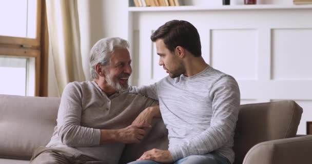 Дружелюбный честный старый отец и маленький сын разговаривают на диване — стоковое видео