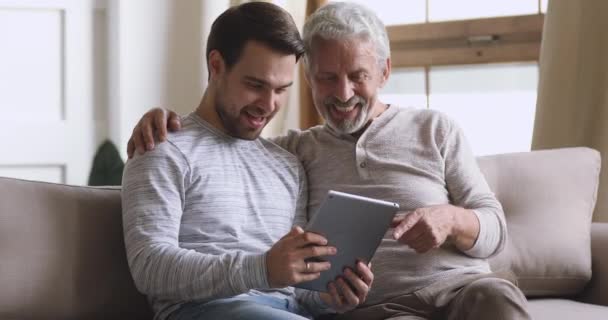 Szczęśliwy starszy ojciec i dorosły syn za pomocą tabletu w domu — Wideo stockowe