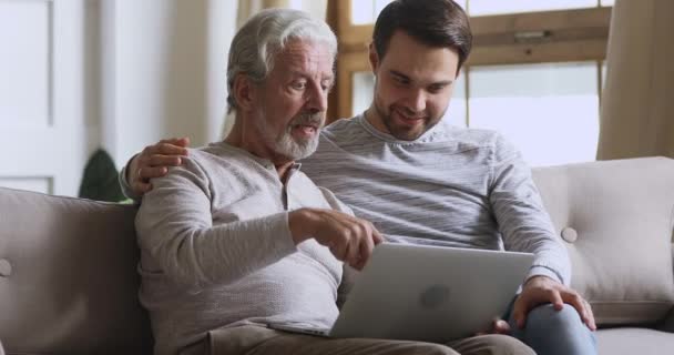 Пожилой отец поговорить с сыном обсудить онлайн новости с помощью ноутбука — стоковое видео
