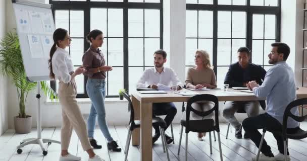 Deux collègues féminines de diverses origines ethniques donnent une présentation commerciale sur un tableau à feuilles mobiles — Video