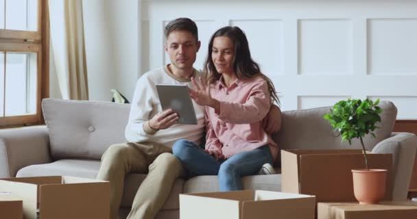 Счастливая пара с помощью планшета говорить на диване в день переезда — стоковое видео