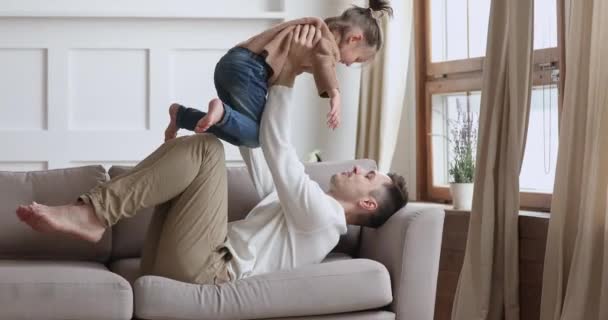 Amoroso pai levantando bonito criança pequena filha brincando no sofá — Vídeo de Stock