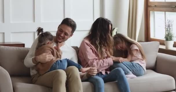 Cheerful parents and cute kids having fun tickling on sofa — Stock Video