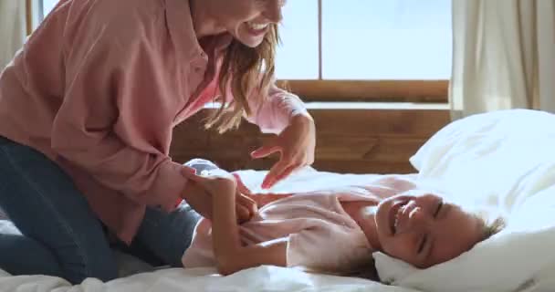 Η παιχνιδιάρα μαμά γαργαλάει την κόρη της γελάει παίζει ξαπλωμένη στο κρεβάτι — Αρχείο Βίντεο