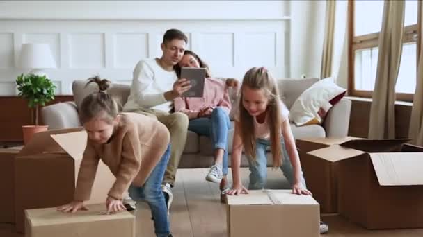 Children playing with boxes parents using tablet on moving day — 비디오