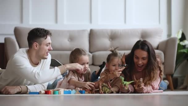 Junge Eltern und niedliche Kinder spielen Dinosaurier auf dem Boden liegend — Stockvideo