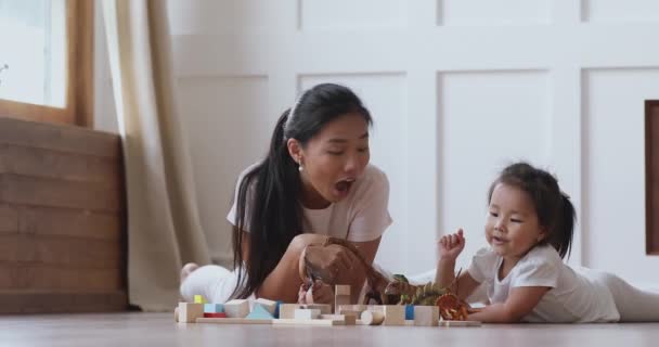 Glad asiatisk mamma och dotter som leker dinosaurier på golvet — Stockvideo
