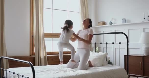 Zorgeloze aziatische kind dochter springen op bed spelen met mam — Stockvideo
