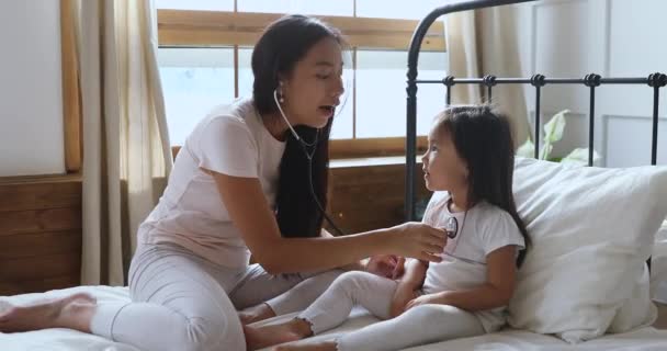 हैप्पी एशियाई माँ और बच्चे बेटी बिस्तर में डॉक्टर खेलते हैं — स्टॉक वीडियो