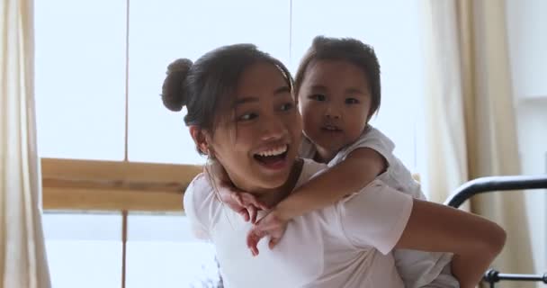 Lächelnd asiatische Mutter huckepack Kind Tochter spielt lachen im Bett — Stockvideo