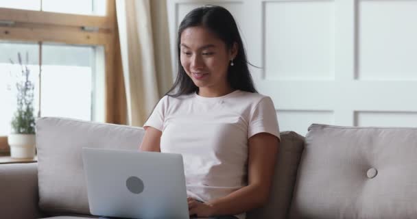 Усміхнена азіатська молода жінка спілкується онлайн за допомогою ноутбука вдома — стокове відео