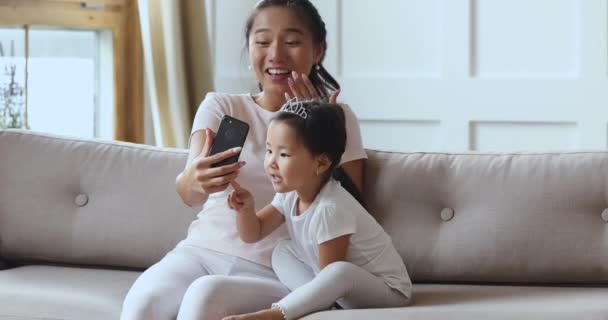 Asian mom and daughter using smartphone funny app on sofa — Stock Video