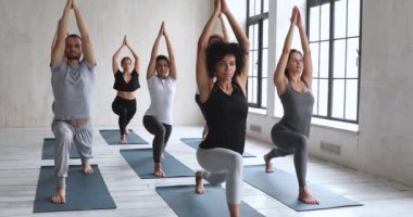 Yoga seansına katılan çeşitli sportif insanlar Virabhadrasana 'yı icra ediyorlar.