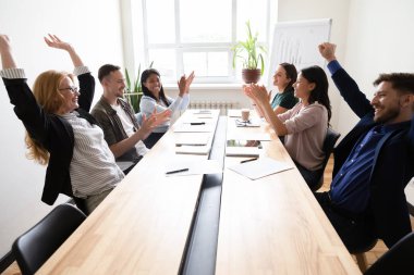 Ortak başarıyı kutlayan şirket çalışanları toplantı masasında oturuyor.